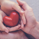 Two hands embracing a small red heart