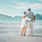 Back, hug or old couple on beach to relax with love, care or support on summer vacation in nature. Retirement, mature man or senior woman at sea or ocean to travel on holiday together looking at view