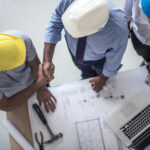 Team of one women architect and two men architects on a construction site. Men are shaking hands. Shot from above.
