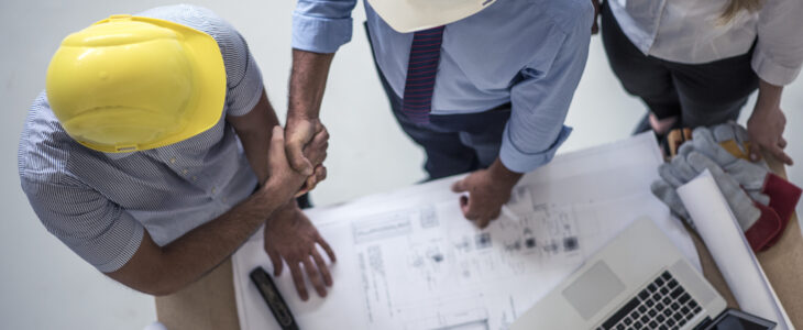 Team of one women architect and two men architects on a construction site. Men are shaking hands. Shot from above.