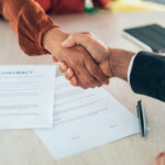 Two professionals shake hands over a signed contract, representing the successful conclusion of a business deal. This image embodies the spirit of collaboration and trust in a corporate environment.